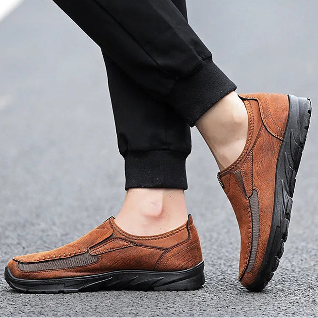 Brown leather shoes worn with black pants on a gray background