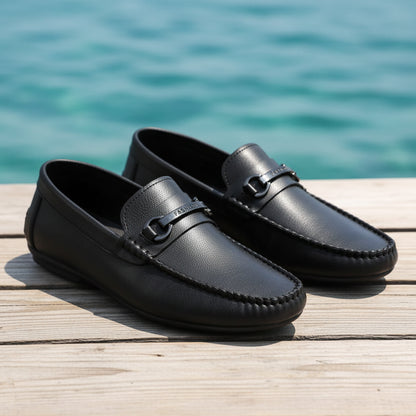 Black leather loafers with a decorative buckle on a textured surface.