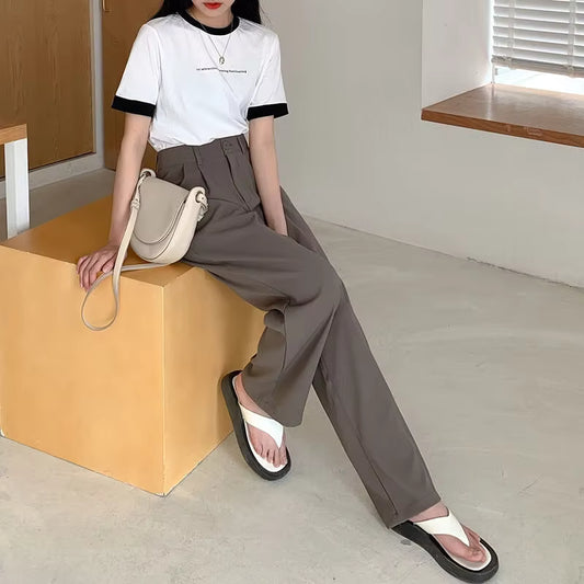 Person sitting on a yellow block holding a beige handbag, wearing a white t-shirt and brown pants.