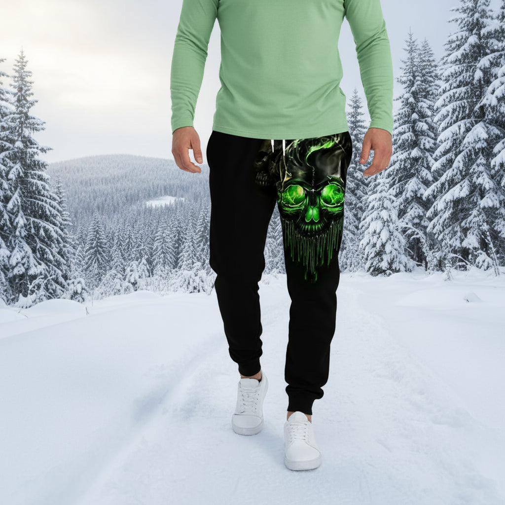 Black jogger pants with green skull design worn by a person on a gray background