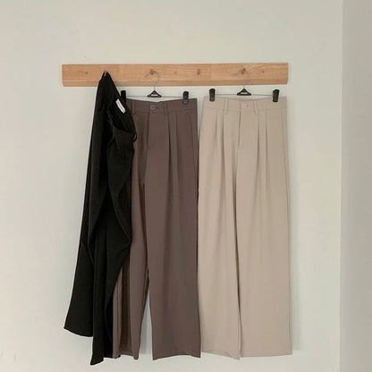 Three pairs of pants hanging on a wooden rack against a white wall.
