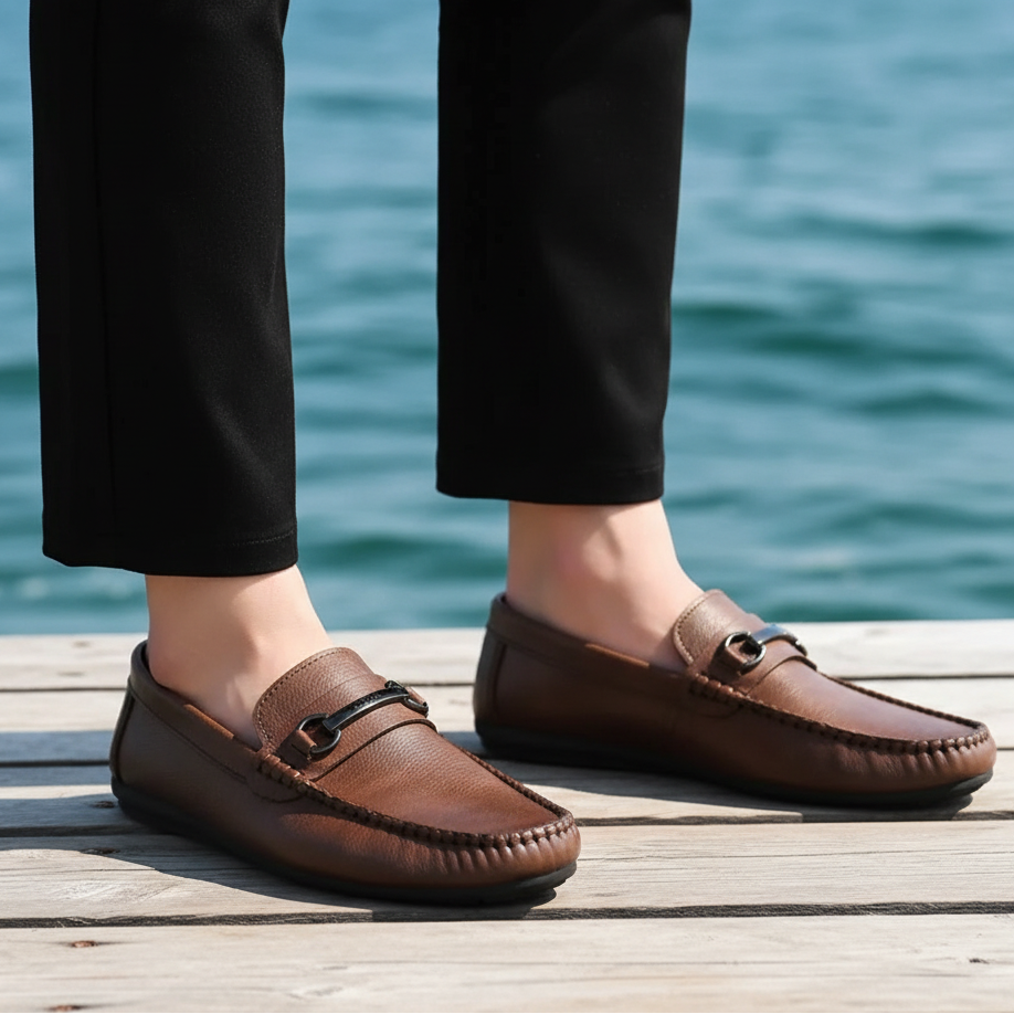 Brown loafers worn with black pants on a blurred indoor background