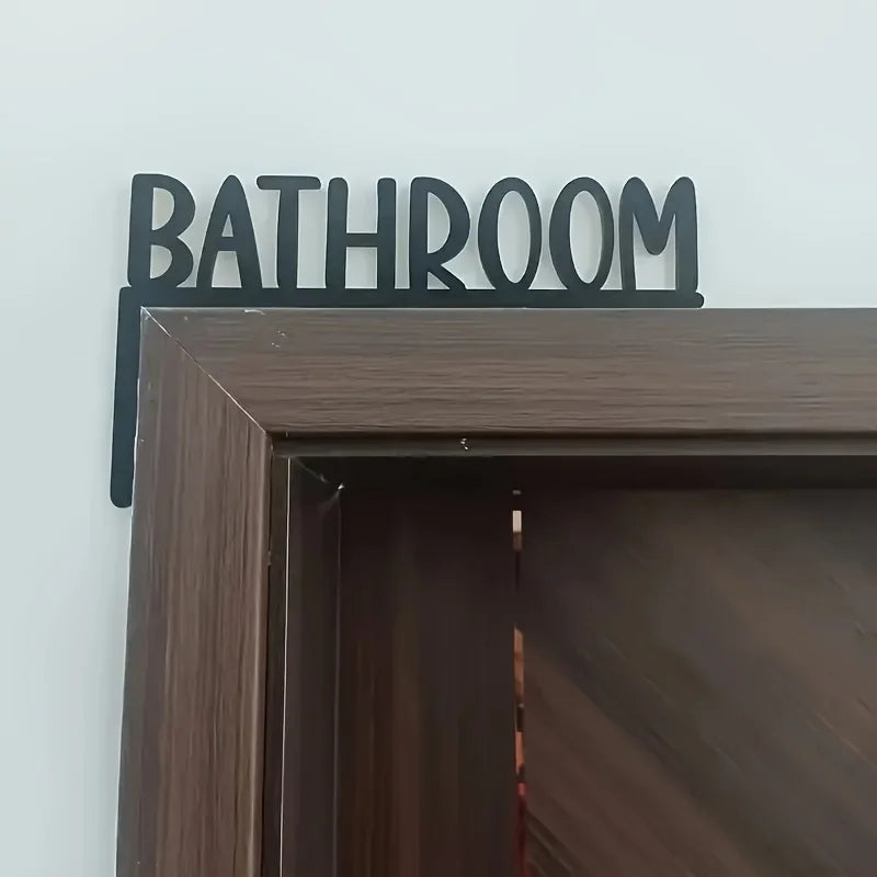 Metal 'Bathroom' sign on a wooden shelf against a white wall