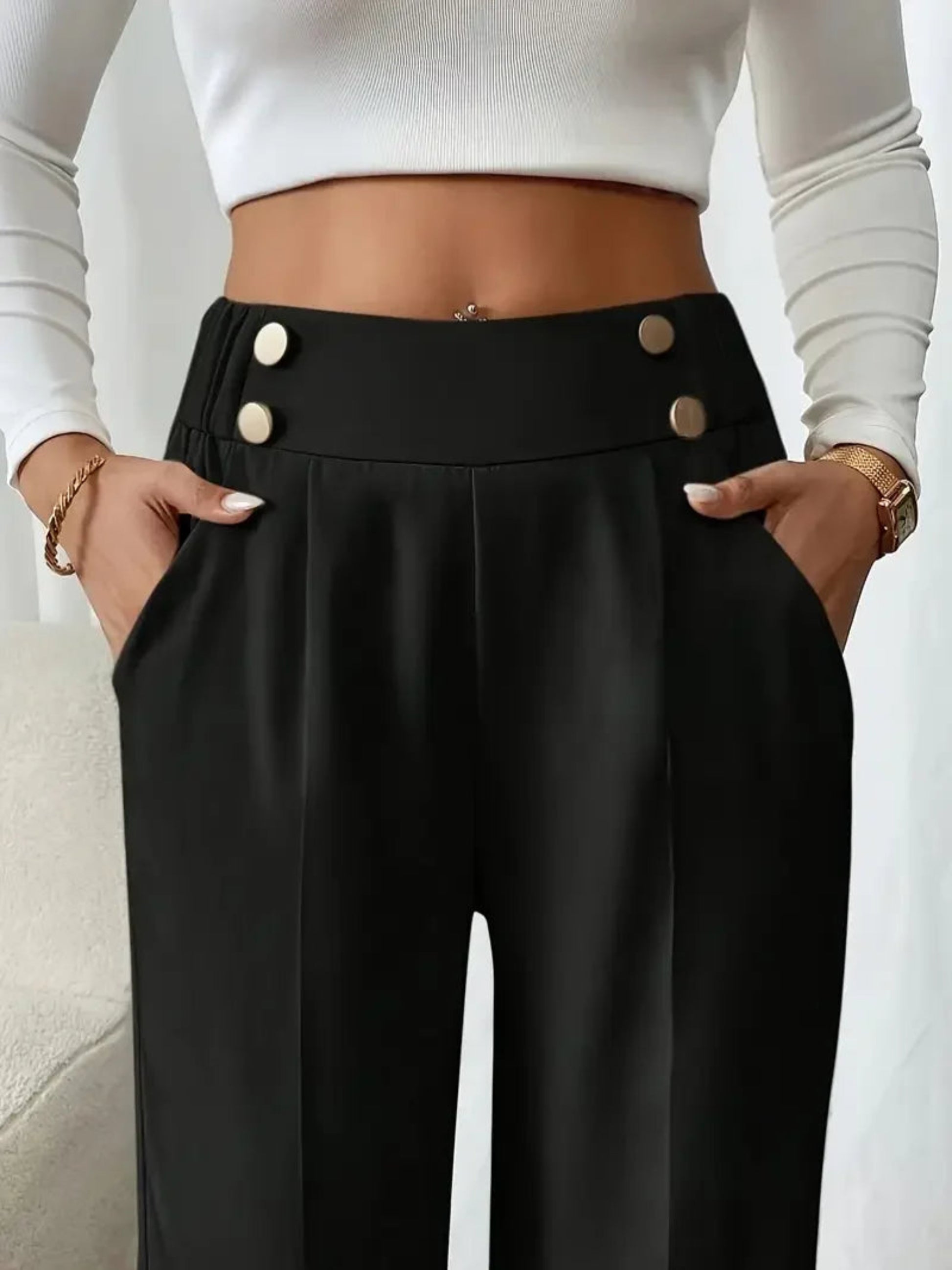 Person wearing black pants with buttons and a white top on a neutral background