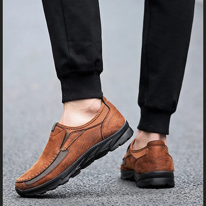 Brown leather shoes worn with black pants on a gray surface
