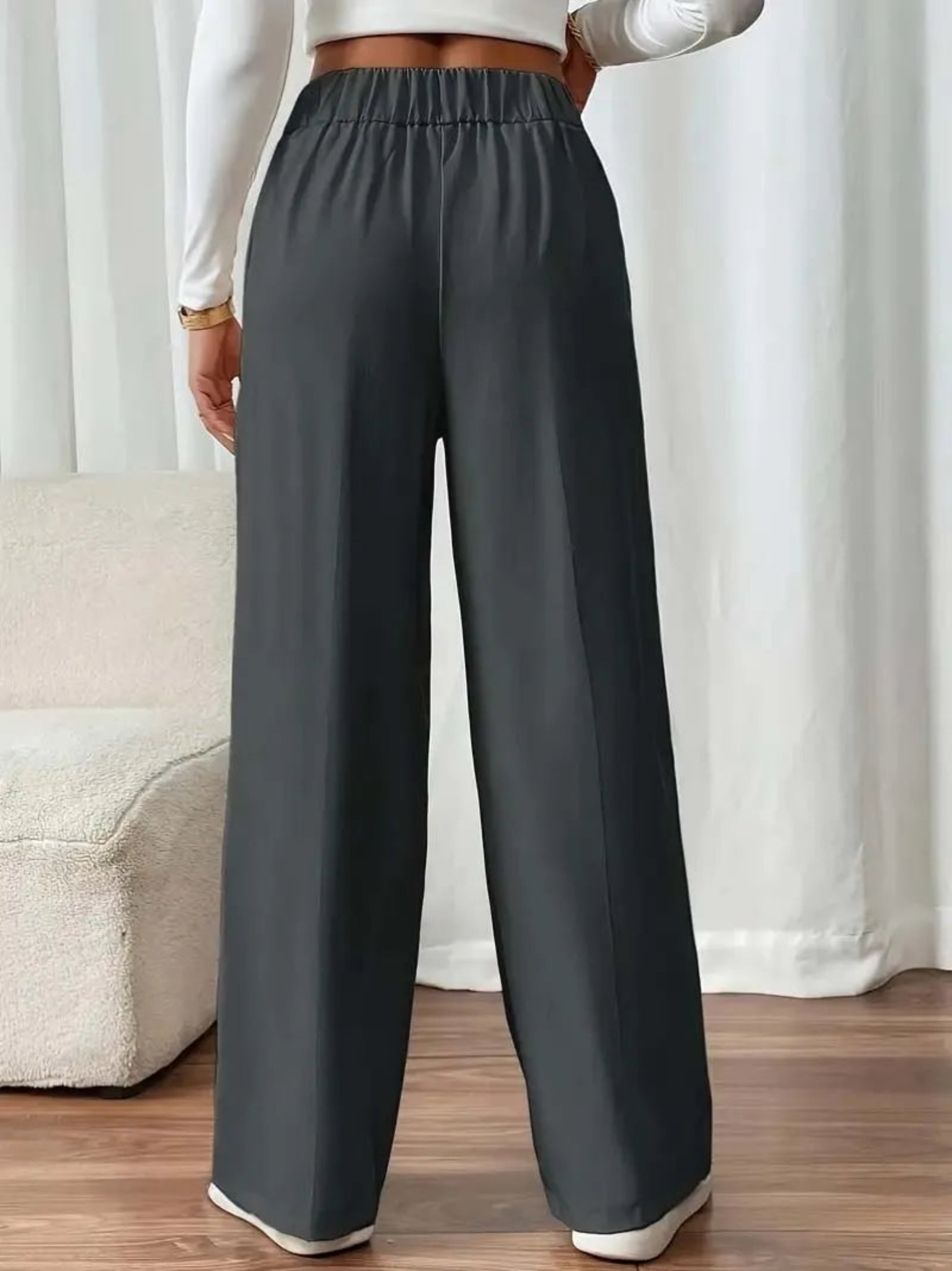 Person wearing dark gray wide-leg pants with a white top and beige sofa in the background.