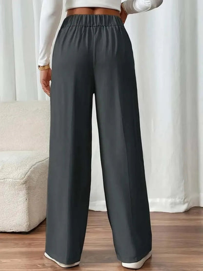 Person wearing dark gray wide-leg pants with a white top and beige sofa in the background.