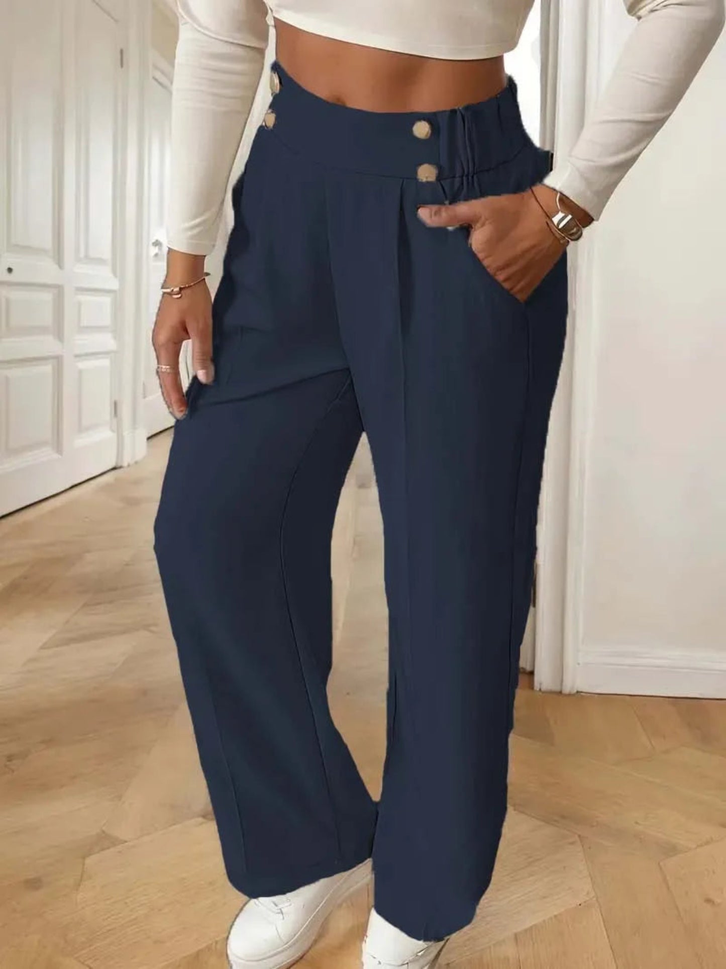 Person wearing navy wide-leg pants with a white top and white shoes indoors.
