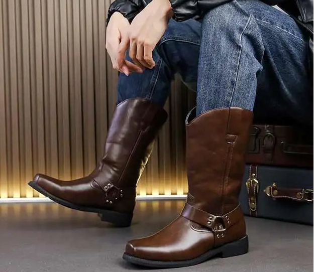 Brown leather boots worn by a person sitting on a bench with a suitcase.