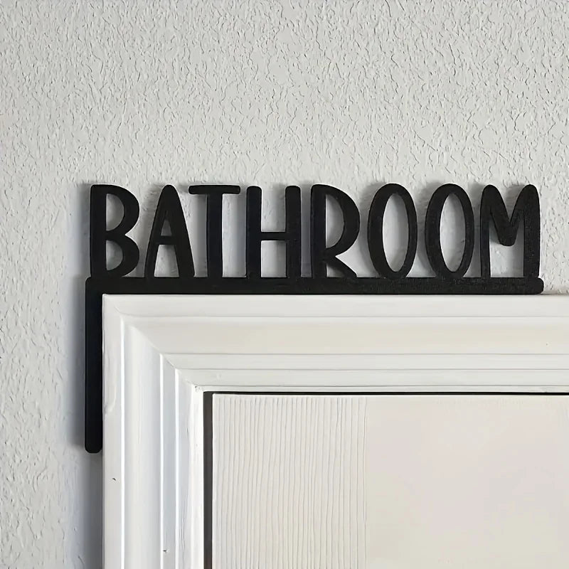 Black 'Bathroom' sign on a white door frame against a light gray wall.