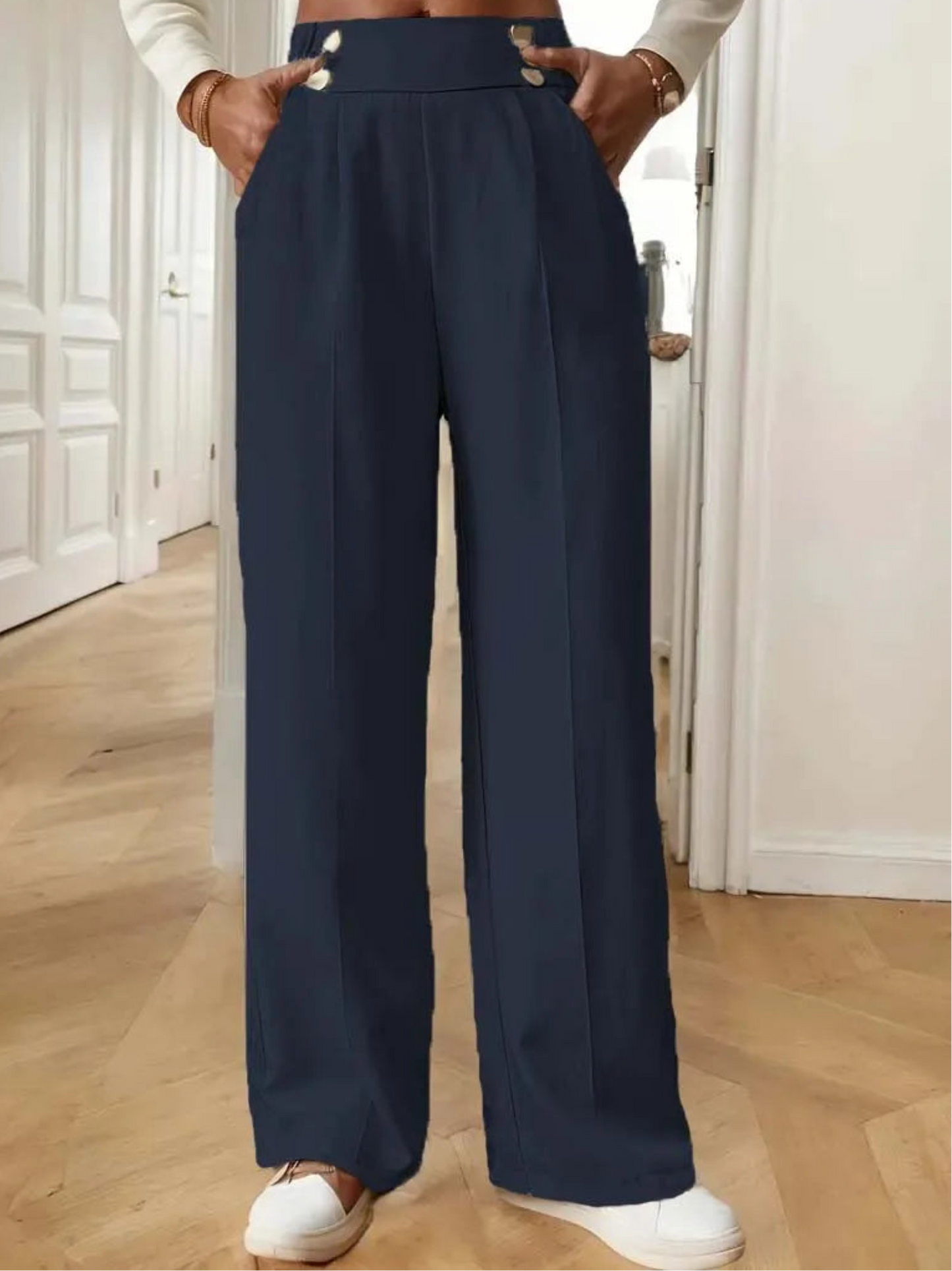 Person wearing navy wide-leg pants with a white top and white shoes indoors.