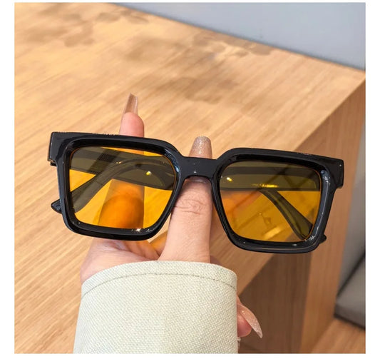 Sunglasses with yellow lenses held by a hand on a wooden surface
