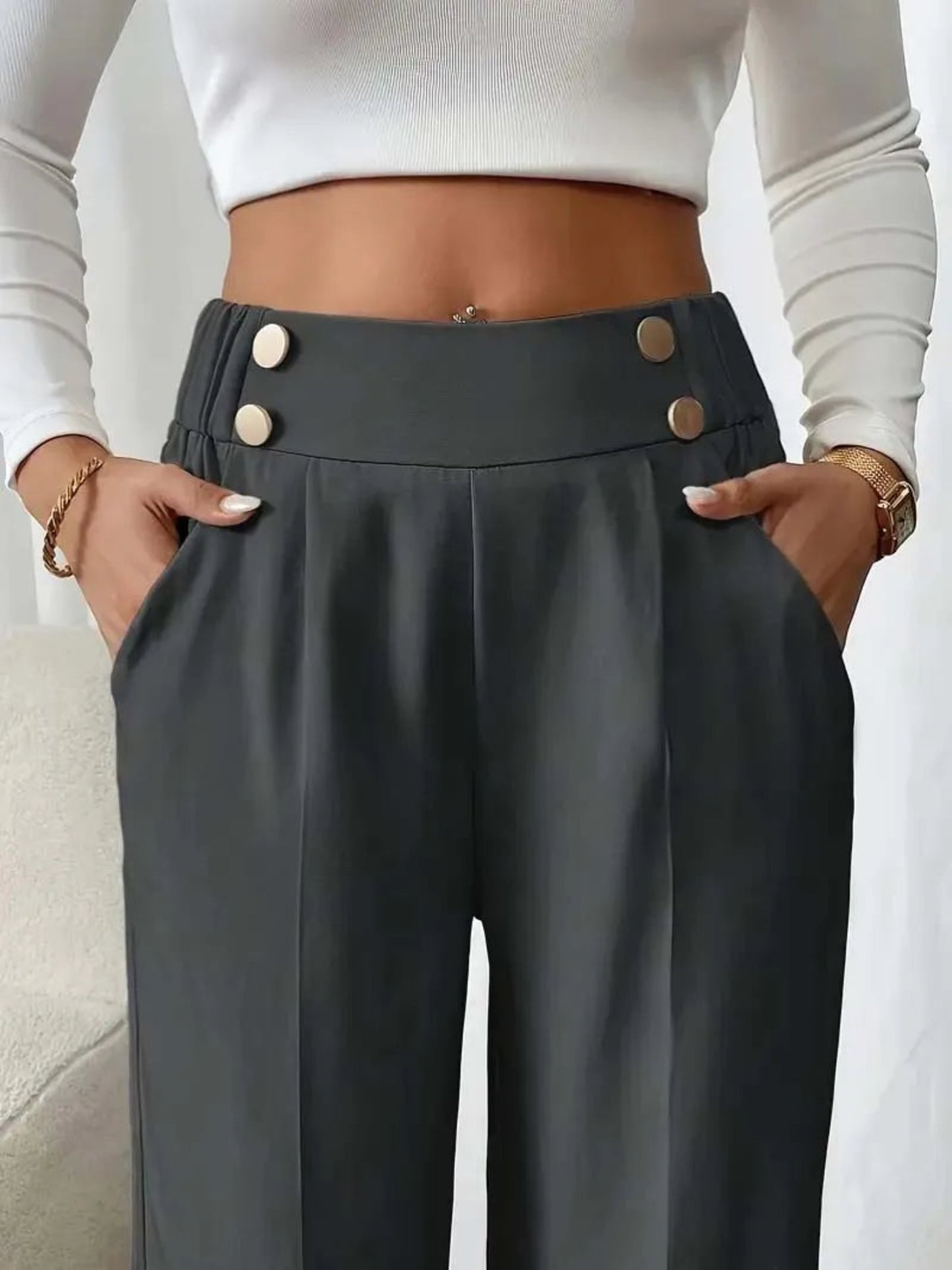Person wearing dark gray pants with button details and a white top.
