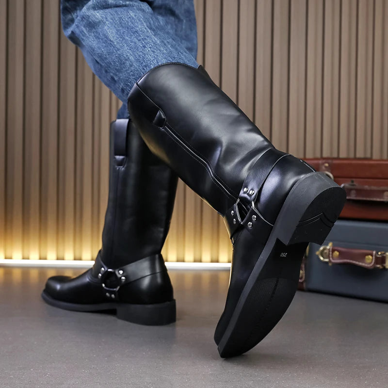 Black leather boots with buckles worn by a person, with suitcases in the background.