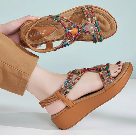 Brown sandals with colorful beading worn by a person on a light blue background