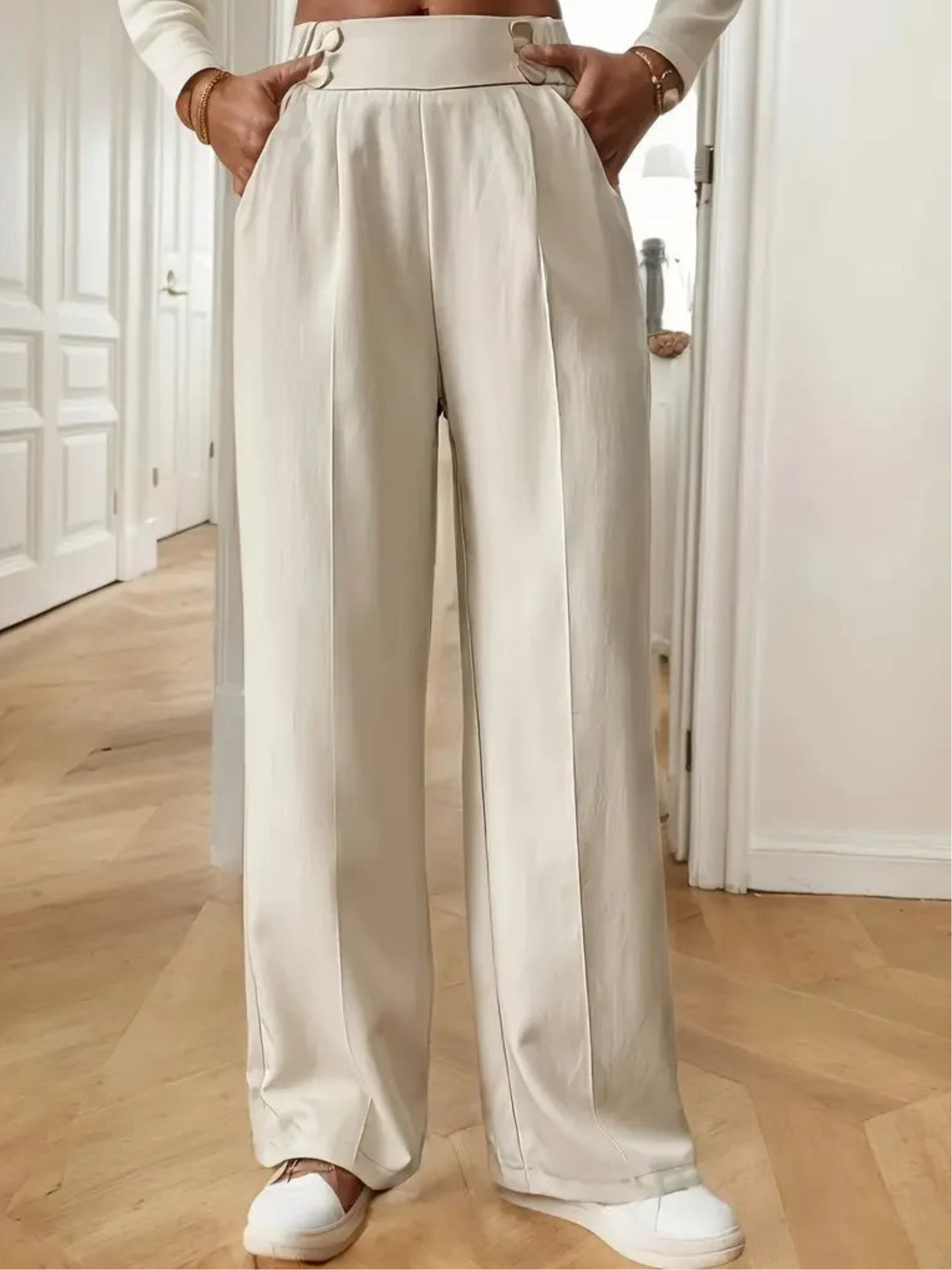 Person wearing beige wide-leg pants and white sneakers in a minimalistic room.