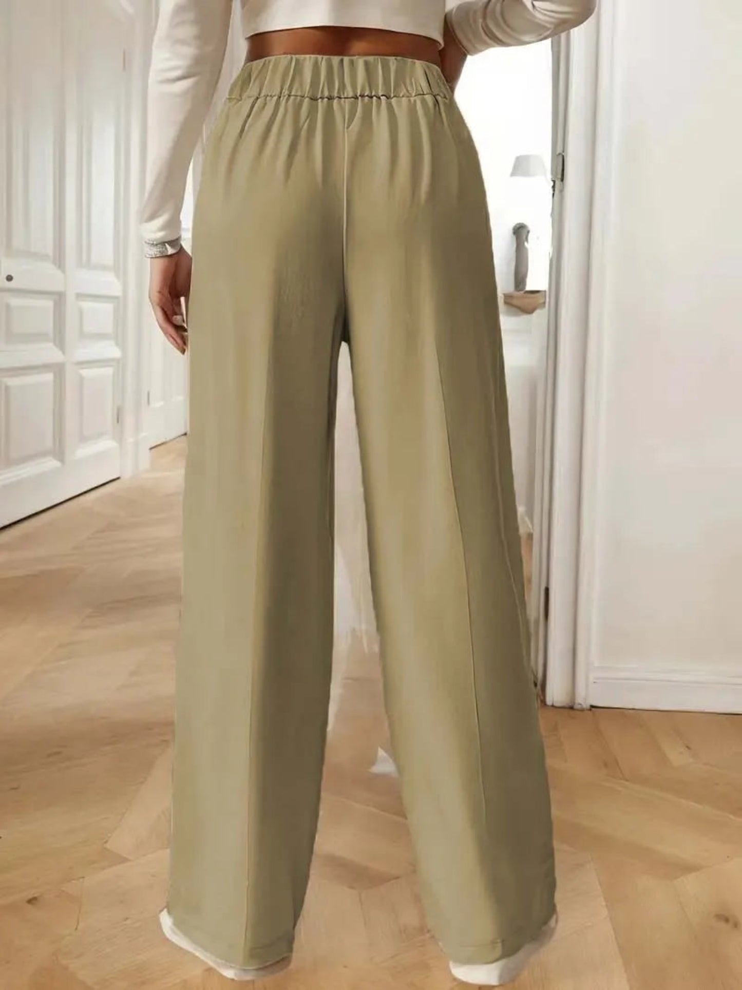 Person wearing light green wide-leg pants in a room with wooden flooring.
