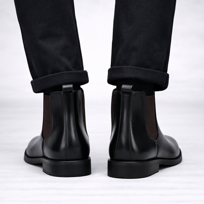 Black leather Chelsea boots worn with black pants on a white background