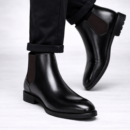 Black leather Chelsea boots worn with black pants on a white background