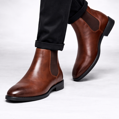 Brown leather Chelsea boots worn with black pants on a white background