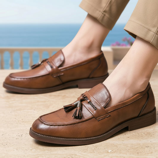 Brown loafers with tassels worn by a person standing on a wooden deck with a scenic background.